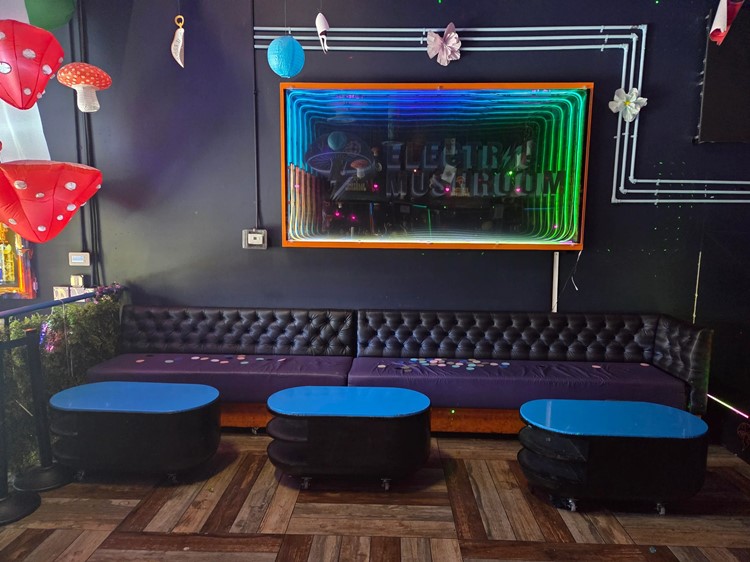 Purple tufted banquette with round blue tables under a mirrored Electric Mushroom sign