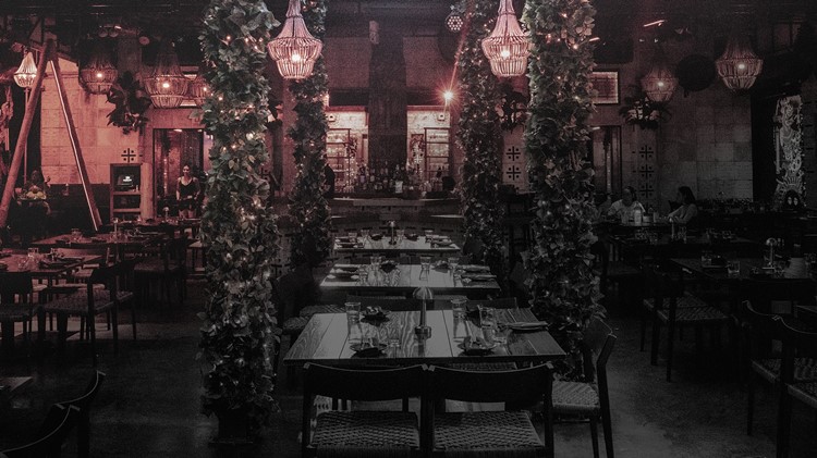 Empty Mayami Wynwood dining courtyard with dark wood tables, greenery-wrapped pillars and lanterns