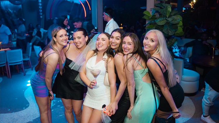 Guests posing inside Mayami Wynwood with plants and blue lit bar behind