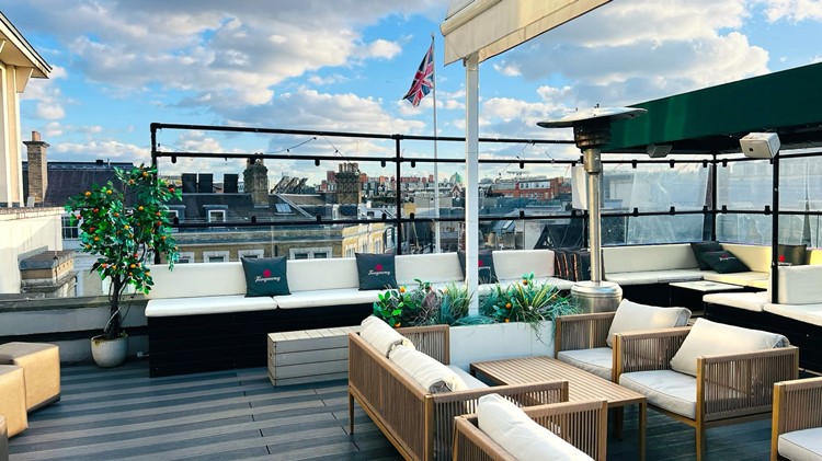 Long white corner sofa with green cushions and wicker armchairs on the Soho Sky Terrace