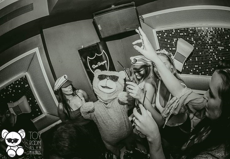 Toy RoOm nightclub Mykonos mascot teddy bear wearing sunglasses having fun with group of girls drinking alcohol