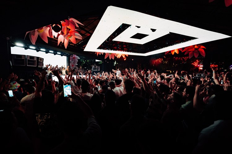 Packed UNO Malta crowd with hands up beneath the white triangular ceiling fixture
