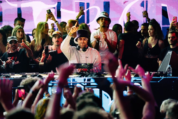 DJ at the decks in the UNO Malta booth with crowd hands in front